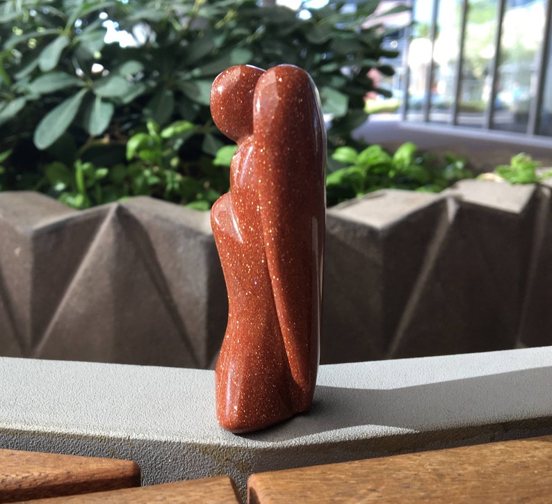 May include: A small, red-brown, carved stone angel figurine with a glittery finish.