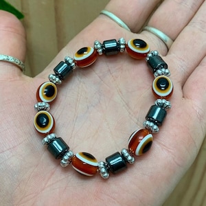 May include: A bracelet with alternating black and silver beads and orange and white eye beads.