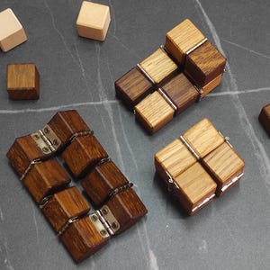 Può includere: Cubetti fidget in legno e blocchi singoli in varie tonalità di legno. I cubetti sono collegati da cerniere metalliche. Alcuni blocchi sono separati, altri sono uniti, creando forme diverse.