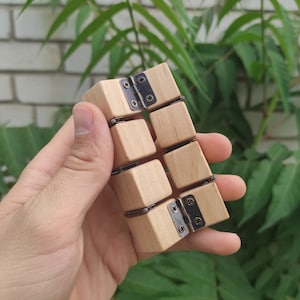 May include: A wooden fidget toy with black metal hinges. The toy is made of six connected cubes that can be flipped and rotated.