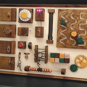May include: A rectangular wooden busy board featuring various tactile elements including four hinged doors with locks, a rotary phone dial, a zipper, a maze with sliding shapes, a lacing panel, a set of wooden blocks, gears, and an abacus.