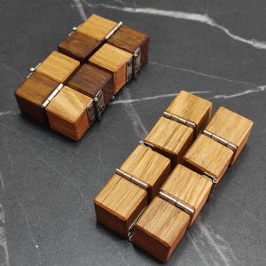 May include: Two wooden fidget cubes with a natural wood grain finish. Each cube is made of eight connected blocks, with silver hinges. One cube has a mix of light and dark wood blocks, while the other is all light wood.