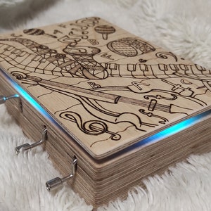 May include: A wooden music box with a hand-drawn design of musical instruments, including a piano, a violin, and a guitar. The box is open and has a blue light shining from the inside. The box has a wind-up key on the side.