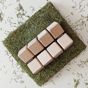 May include: A set of six wooden blocks arranged in a staggered pattern on a bed of green pine needles. The blocks are a light brown colour and have a smooth, natural finish.