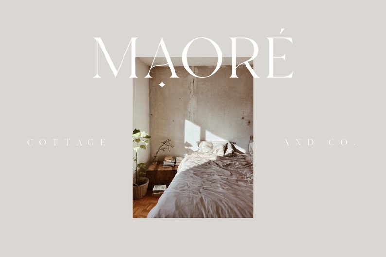 May include: A bedroom interior with a bed made with a light brown linen duvet and pillows. The bed is in front of a concrete wall with a window letting in sunlight. A small plant is in a pot on the floor next to a wooden nightstand with books and a vase with branches. The text "MAORE'" is at the top of the image and "COTTAGE AND CO." is at the bottom.