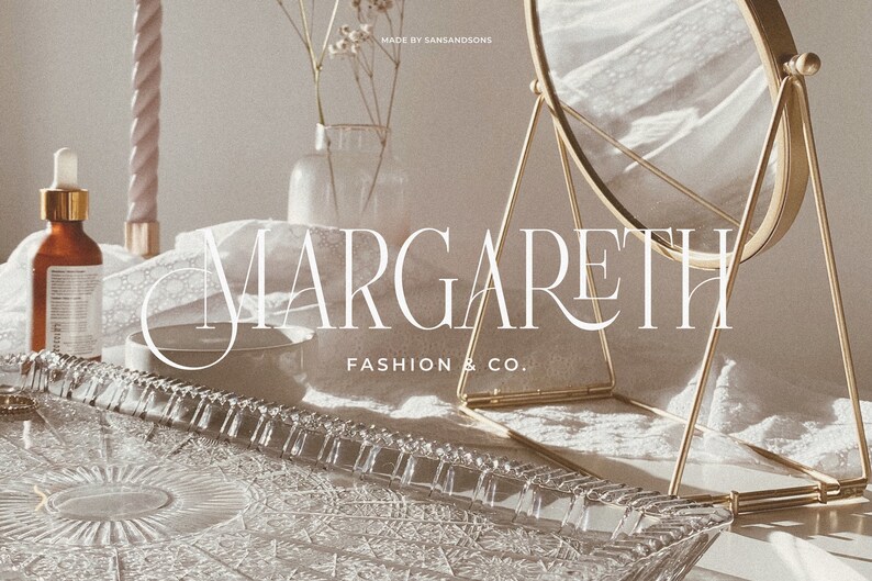 May include: A white text logo on a white background reads "MARGARETH FASHION & CO.". The logo is displayed on a glass tray with a decorative pattern. A gold metal stand with a round mirror is in the background.