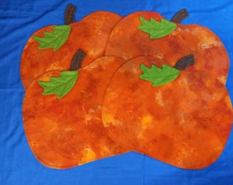 May include: Set of four orange pumpkin-shaped fabric placemats with green felt leaves. The placemats have a mottled orange and yellow pattern.
