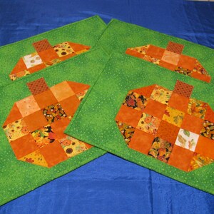 May include: Four green placemats with orange pumpkin designs. Each pumpkin is made of patchwork fabric with various fall-themed prints.