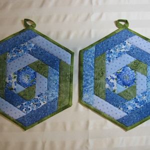 May include: Two blue and green quilted pot holders with a hexagonal shape and a loop for hanging.