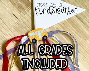 以下が含まれることがあります： 「FIRST DAY OF Kindergarten」の文字が入った白い三角旗が木の棒に付いています。旗の下には黄色のスクールバスが取り付けられています。「ALL GRADES INCLUDED」の文字が下にあります。カラフルなリボンが棒に付いています。