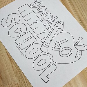 May include: Black and white line art coloring page with the words "back to school" and images of a pencil, ruler, and apple.