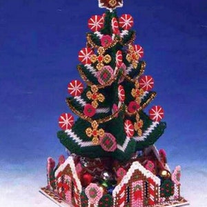 May include: A green Christmas tree candy holder with a gingerbread house base. The tree is decorated with red and white candy canes, pink flowers, and gold glitter. The gingerbread house has red and white candy cane trim and a white roof. "Christmas Tree" Candy Holder. Finished Size: 6" x 13"