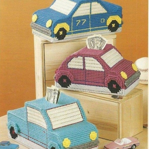 Puede incluir: Tres huchas hechas a mano con forma de coche en azul, morado y azul claro, cada una con una ranura para insertar dinero. Las huchas tienen marcos de ventanas blancos, faros amarillos y ruedas negras. Se ven billetes en las ranuras.