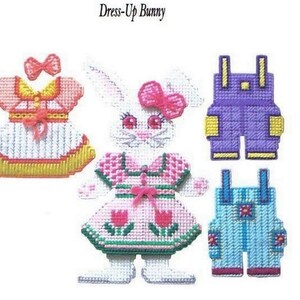May include: Dress-Up Bunny craft kit featuring a white bunny with pink and green dress, a pink dress with yellow trim, purple overalls with yellow trim, and blue overalls with red trim.