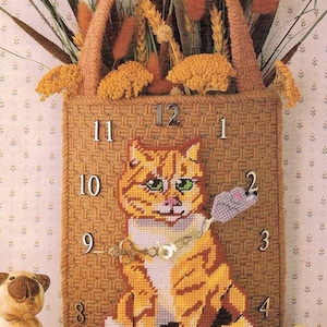 May include: A handcrafted, orange tabby cat clock with a woven texture. The clock features a cat holding a gray mouse, with numbers marking the hours. The clock is part of a decorative wall hanging with a woven handle and floral accents.