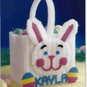 May include: White plastic Easter basket shaped like a bunny with pink ears and blue eyes. The basket has a handle and is decorated with colorful Easter eggs and the name "KAYLA".