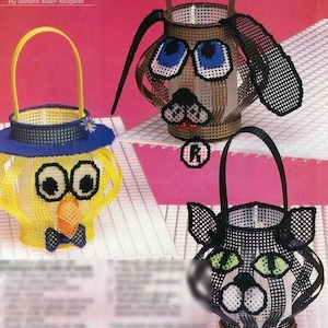 May include: Three plastic canvas baskets with animal faces. The baskets are yellow, brown, and black. The yellow basket has a blue hat and a bow tie. The brown basket has a dog face with blue eyes. The black basket has a cat face with green eyes. The baskets are all decorated with colorful beads.