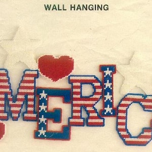 May include: A wall hanging with the word "America" spelled out in blue and red letters. The letters are decorated with white stars and red and white stripes, resembling the American flag. Two red hearts are also included in the design.