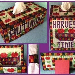 May include: A collection of fall-themed, cross-stitched tissue box covers and accessories. The designs feature a basket of red apples, green leaves, and the words "AUTUMN" and "HARVEST TIME". The color scheme includes red, green, brown, and cream.