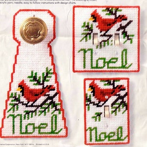 Puede incluir: Un conjunto de tres cubiertas navideñas de punto de aguja. El conjunto incluye una cubierta para el pomo de la puerta y dos cubiertas para los interruptores de la luz. Cada cubierta presenta un cardenal rojo, follaje verde y la palabra "Noel" en verde.