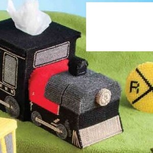 以下が含まれることがあります： 黒、赤、グレーの電車型のティッシュボックスで、上から白いティッシュが出ています。ティッシュボックスの隣には、黒い文字が入った黄色の踏切標識があります。ティッシュボックスには車輪と煙突が付いています。