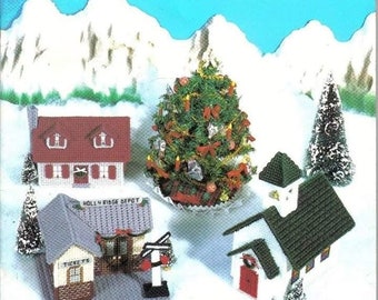 May include: A craft pattern book titled "THE VILLAGE" featuring needlework designs for plastic canvas. The cover displays a miniature village scene with houses, a train, and a Christmas tree. The text "HOLLY RIDGE DEPOT" is visible. Designed by Nancy Dorman.