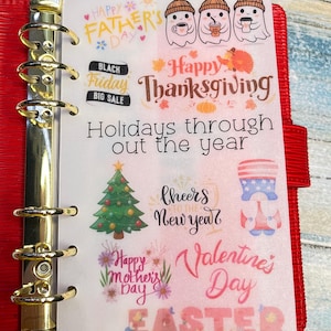 May include: A red planner with gold rings, open to a page of holiday-themed stickers. The stickers include text for Father's Day, Black Friday, Thanksgiving, Christmas, New Year, Mother's Day, Valentine's Day, and Easter.
