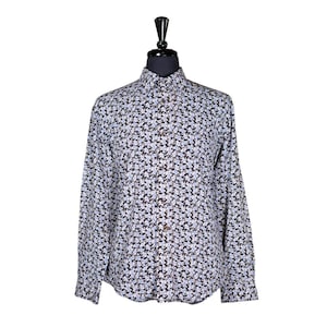 Puede incluir: Una camisa de manga larga con botones, fondo blanco y un pequeño estampado floral azul y negro.