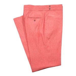 May include: Coral-colored pants with a textured, woven fabric. The pants have a button and zipper closure, a small pocket, and two buttons on the back. The pants are folded and displayed against a white background.