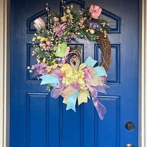 May include: A spring wreath with pastel pink, yellow, and blue ribbon bows. The wreath is decorated with artificial flowers, greenery, and Easter eggs.