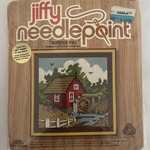 May include: A Jiffy Needlepoint kit titled "Summer Mill" designed by Barbara Jennings. The kit features a cross-stitch design of a red mill house with a water wheel, set against a blue sky and green trees. The kit includes a printed design, yarn, and instructions.