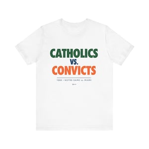 Puede incluir: Camiseta blanca con texto verde, naranja y azul que dice "Catholics vs. Convicts 1988 Notre Dame vs. Miami".