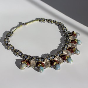 Puede incluir: Un collar de cuentas con una cadena plateada y gris y cuentas de color marrón, transparente y azul en forma de lágrima.