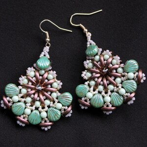 May include: A pair of dangle earrings with a green and white beaded design. The earrings are made with small, round beads and larger, shell-shaped beads. The beads are arranged in a circular pattern, creating a floral-like design.