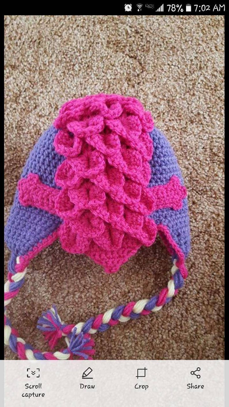 May include: A pink and purple crocheted hat with a braided strap. The hat has a unique design with a textured pattern.