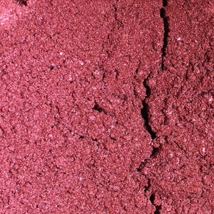 May include: Close-up of a deep red, sparkly, fine-grained powder. The powder has a slightly textured surface and a crack running through the center.