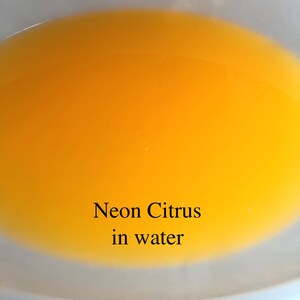 May include: A close-up of a clear bowl filled with bright yellow liquid. The text "Neon Citrus in water" is written below the bowl.