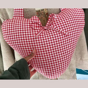 Peut inclure: Un coussin en forme de cœur à carreaux rouges et blancs, orné d'un nœud. Le coussin est doté d'une poignée et est un objet décoratif. Le tissu est doux.