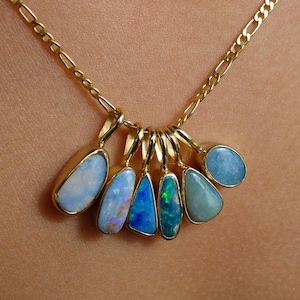 Pode incluir: Um colar de corrente de ouro com seis pingentes individuais, cada um cravejado com uma gema de opala de formato irregular. As opalas exibem vários tons de azul, branco e verde com flashes iridescentes, em engastes de ouro polido.