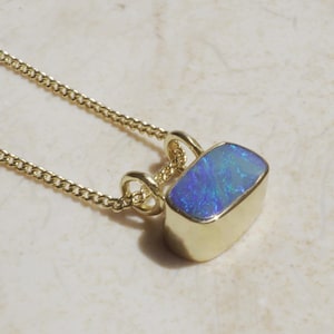 Peut inclure: Un collier en or avec un pendentif rectangulaire orné d'une opale bleue et verte. Le pendentif est serti dans de l'or et suspendu à une fine chaîne en or. L'opale présente un jeu de couleurs.