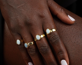 May include: Four gold rings, each featuring a single, smooth, oval-shaped white stone set in a polished metal band. The rings are worn on the fingers, showcasing a consistent design with a reflective gold finish and a milky, opaque white gemstone.
