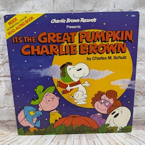 May include: A Charlie Brown Records vinyl album cover titled It's the Great Pumpkin, Charlie Brown by Charles M. Schulz. The purple cover features Snoopy in a pilot hat, Charlie Brown, and friends in Halloween costumes against a large yellow moon.