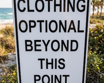 May include: A white rectangular sign with black text that reads "CLOTHING OPTIONAL BEYOND THIS POINT." The sign is mounted on a wooden post, with a beach and ocean in the background.