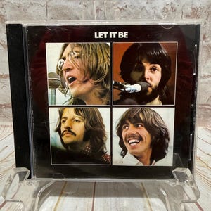 Op de afbeelding: Een cd-hoesje met de albumhoes van "Let It Be" van The Beatles. De hoes toont vier individuele portretten van de bandleden. De albumtitel staat in het wit bovenaan de hoes.