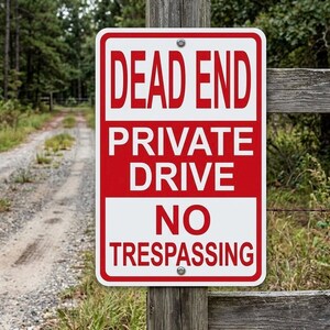 May include: A rectangular red and white sign with the words "DEAD END PRIVATE DRIVE NO TRESPASSING" in bold, capital letters. The sign is mounted on a wooden post and is in front of a dirt road.