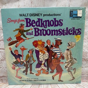 May include: A square vinyl record cover for Walt Disney productions' Songs from Bedknobs and Broomsticks. The light blue cover features colorful illustrations of characters including a flying person on a broom, a lion, a bear, and a suit of armor.