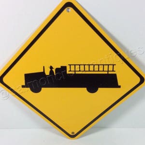 May include: Yellow diamond-shaped road sign with a black silhouette of a fire truck with a ladder on top. The sign warns drivers to be aware of fire trucks.