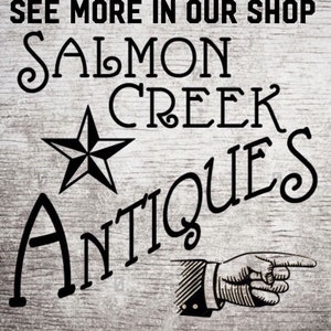 May include: Black and white sign with the text "Salmon Creek Antiques" in a stylized font. A five-pointed star is above the text, and a pointing hand is below the text. The sign says "See more in our shop" at the top.