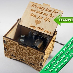 May include: A wooden music box with a floral design on the outside. The lid is open and has a personalized message engraved on the inside: "It's only him for me and me for him, for life." The message is followed by "Song Title Here".