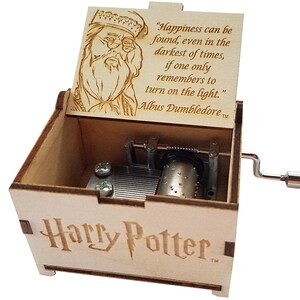 May include: A wooden music box with a hand-crank on the side. The lid is open and features an engraved image of Albus Dumbledore with a quote from the Harry Potter series: "Happiness can be found, even in the darkest of times, if one only remembers to turn on the light."  Albus Dumbledore. The bottom of the box is engraved with "Harry Potter".